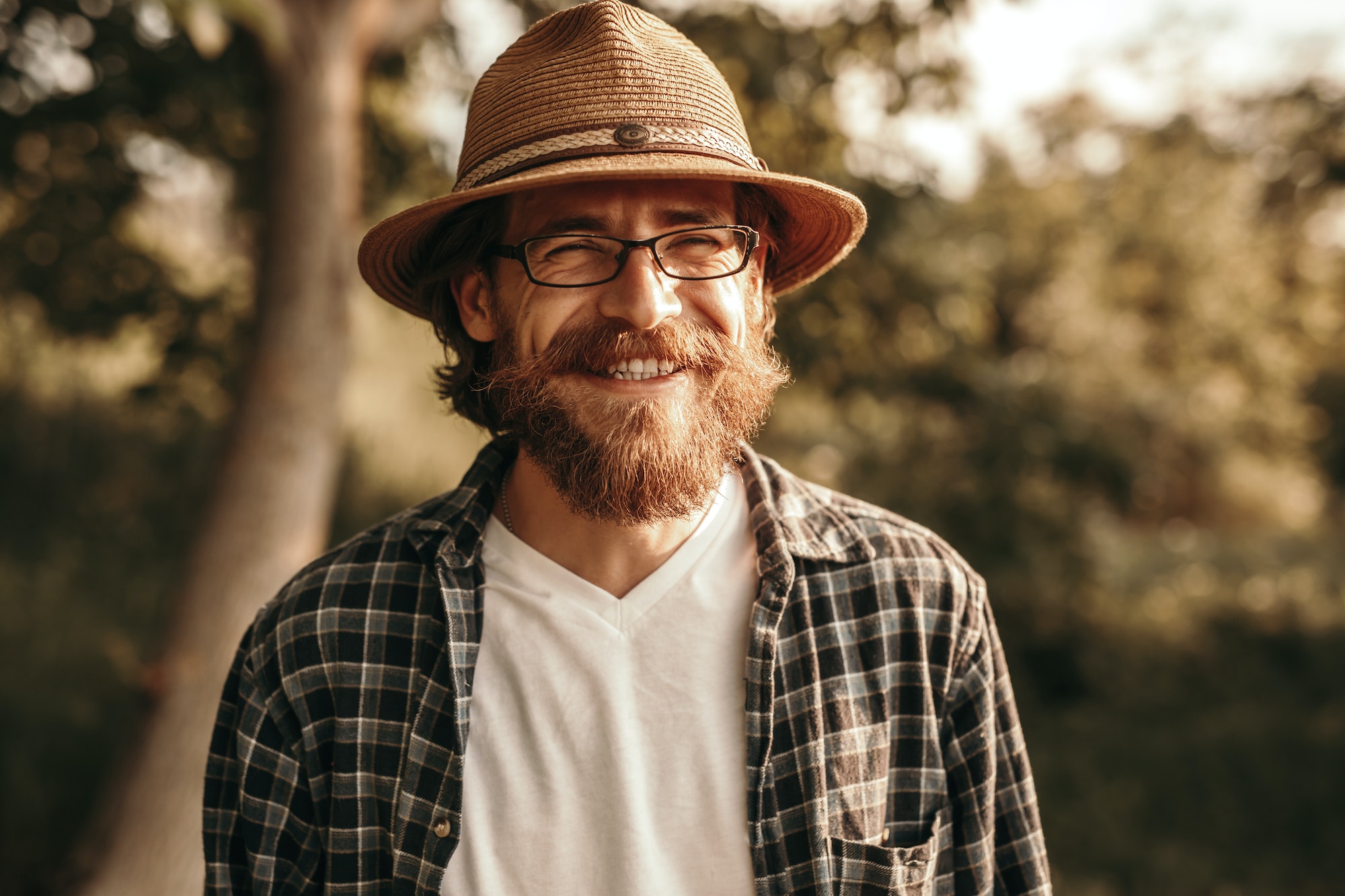 Smiling bearded man in glasses and hat in nature